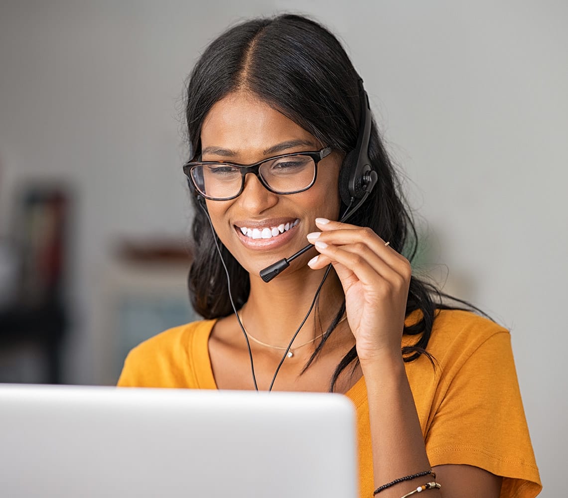A person wearing glasses and a headset smiles while looking at a laptop screen.